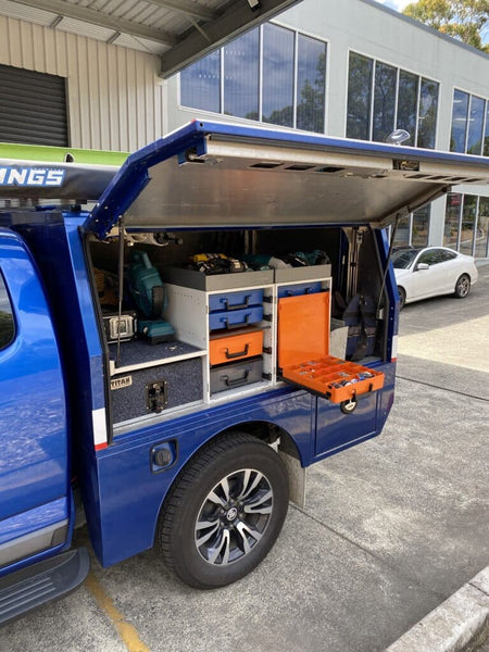 Blue van with open cargo area showing organized tools and equipment outside a building.